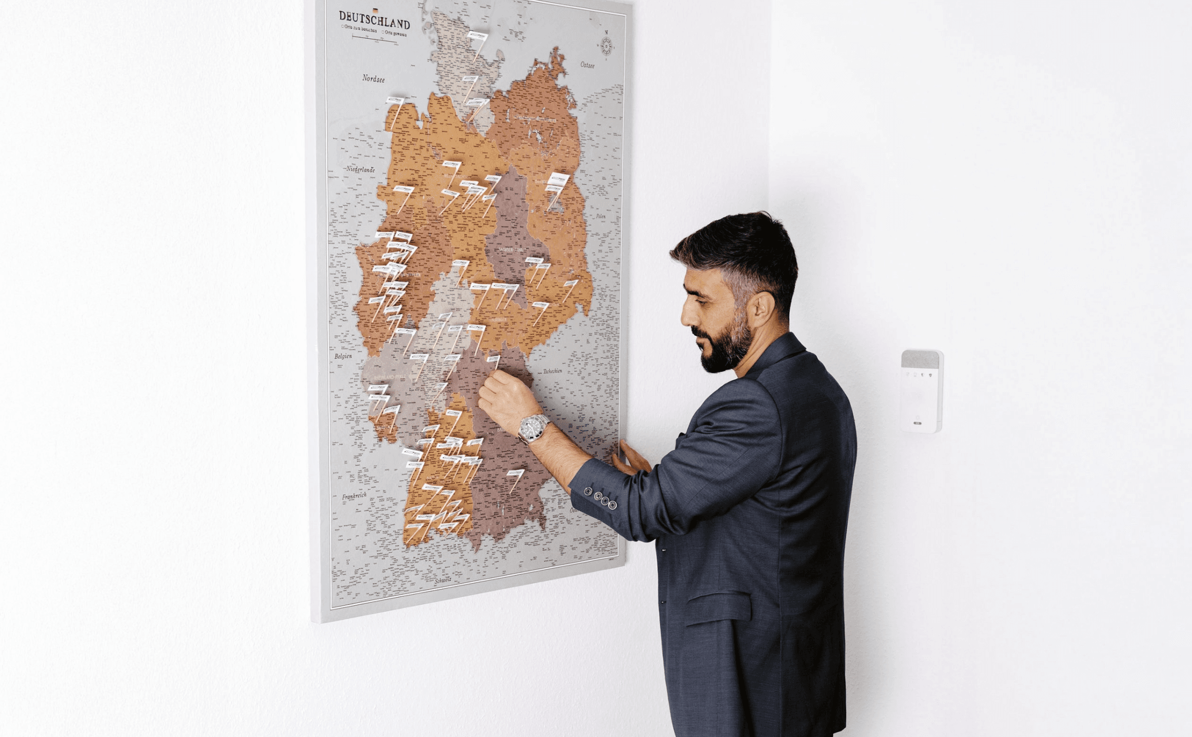 Ein bärtiger Mann im Anzug steckt eine weiße Fahne auf eine Deutschlandkarte an der Wand.